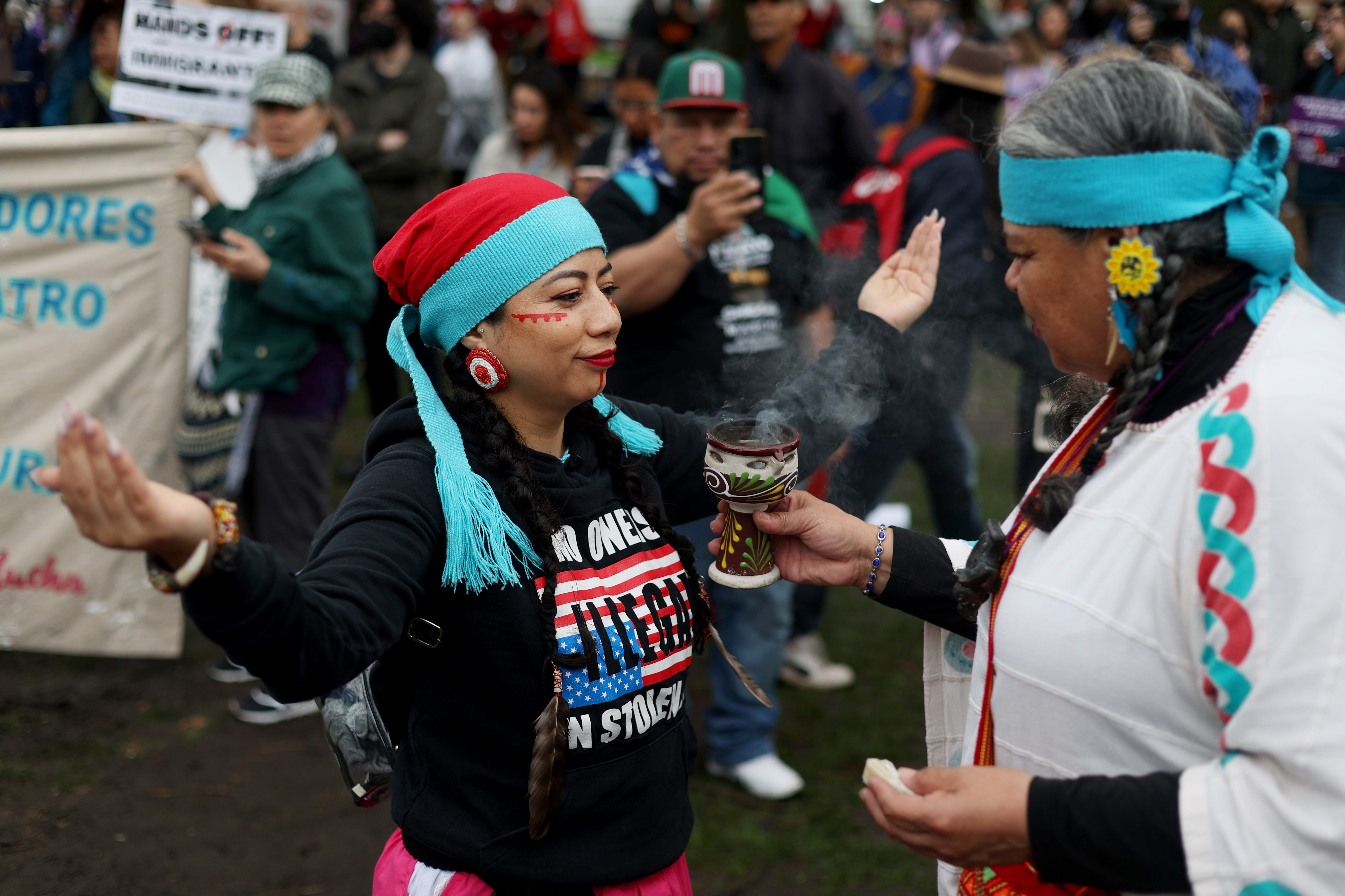 Ollin Kuikatl Tekpatl, left, performs smudging, using medicine to "help harmonize the soul and spirit," on Susana Huitron as hundreds gather at Union Park for the May Day march, May 1, 2025, honoring working people for International Workers' Day, before marching to Grant Park. (Audrey Richardson/Chicago Tribune)