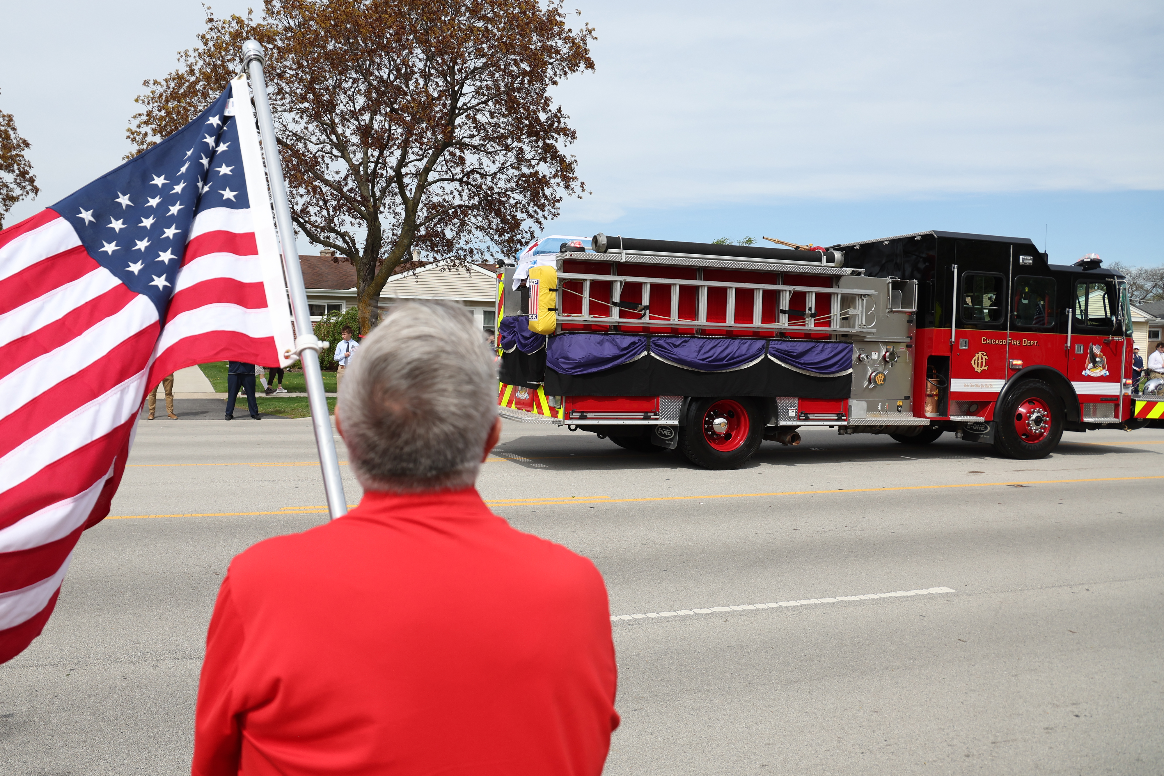 A man holds an American flag as a Chicago fire truck carrying the casket of Chicago Fire Department Capt. David Meyer leaves for St. John Brebeuf Church in Niles, on April 29, 2025. (Antonio Perez/Chicago Tribune)